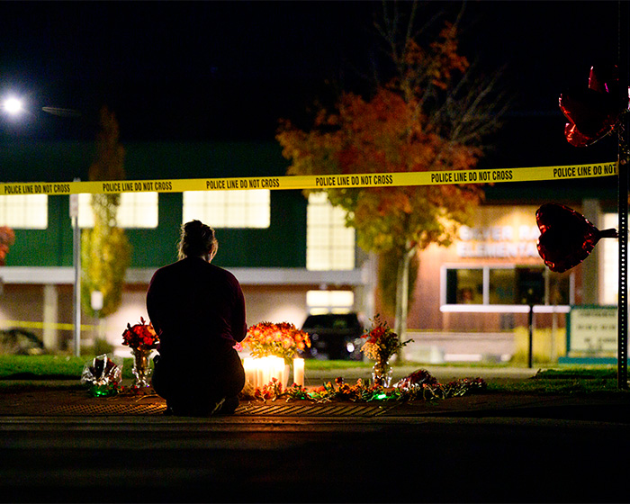 Person sitting in front of candle memorial behind police line at Oregon elementary school tragedy site Person sitting in front of candle memorial behind police line at Oregon elementary school tragedy site