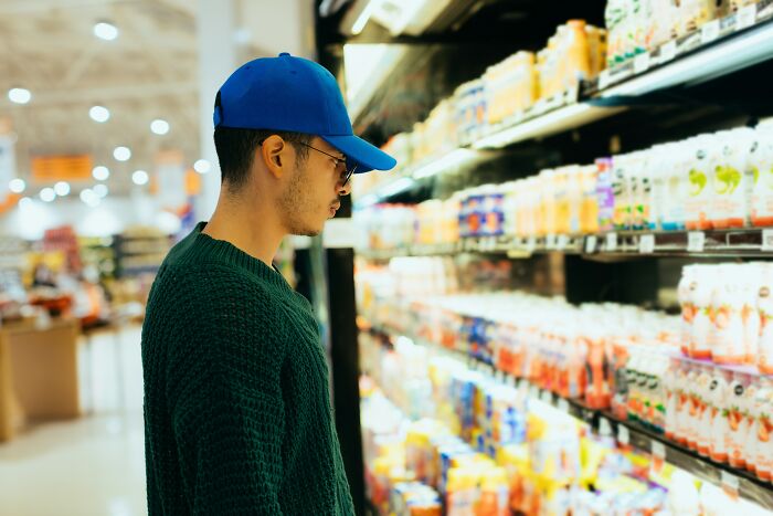 A man wearing a blue cap browsing items on a grocery store shelf in a tiny community.