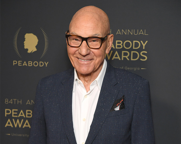 Patrick Stewart smiles in a dark suit jacket and glasses at the Peabody Awards.