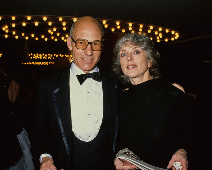 Patrick Stewart wears glasses and a tuxedo while standing next to Sheila Falconer.