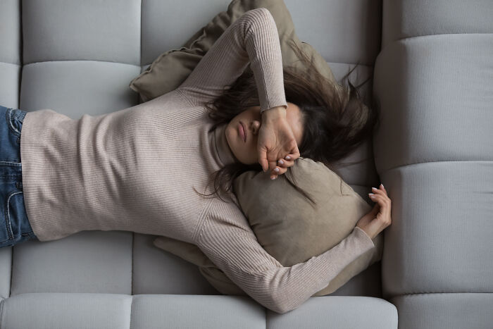 A woman lying on a sofa with her arm over her face, highlighting chronic health problems.