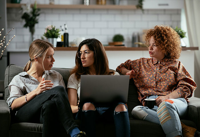 Three roommates having a tense discussion on a sofa with a laptop. Three roommates having a tense discussion on a sofa with a laptop.