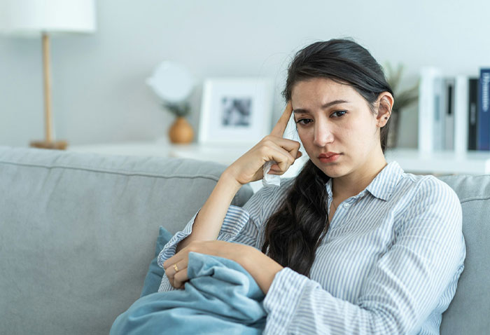 An anxious and stressed woman sitting on a couch, representing the conflict with her roommates. An anxious and stressed woman sitting on a couch, representing the conflict with her roommates.