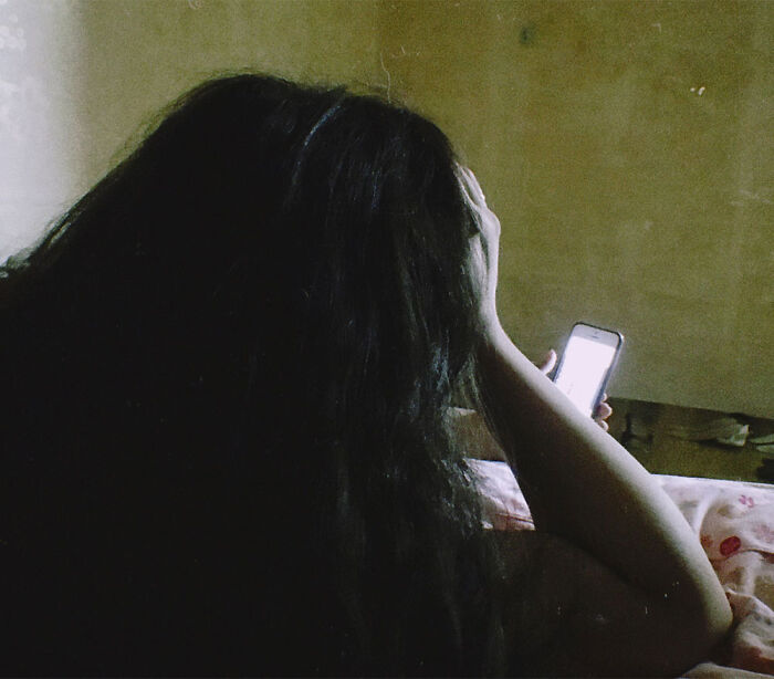 A teen girl lying in bed looking at her brightly glowing smartphone screen.