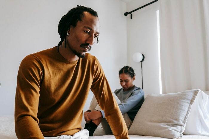 A sad man sitting on the bed with his wife behind him, thinking about whether to walked away from marriage.