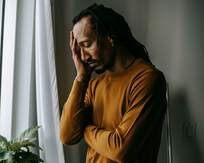 A man with dreadlocks holding his head in stress, representing deep personal secrets.