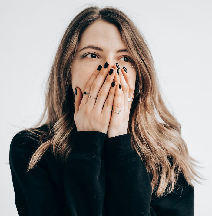 A young woman laughing nervously behind her hands following an embarrassing moment