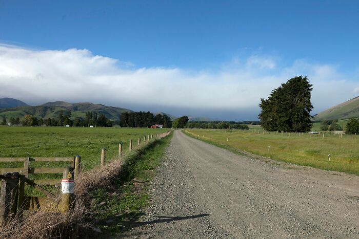 A long gravel road passing through green fields in tiny communities with mountains in the distance