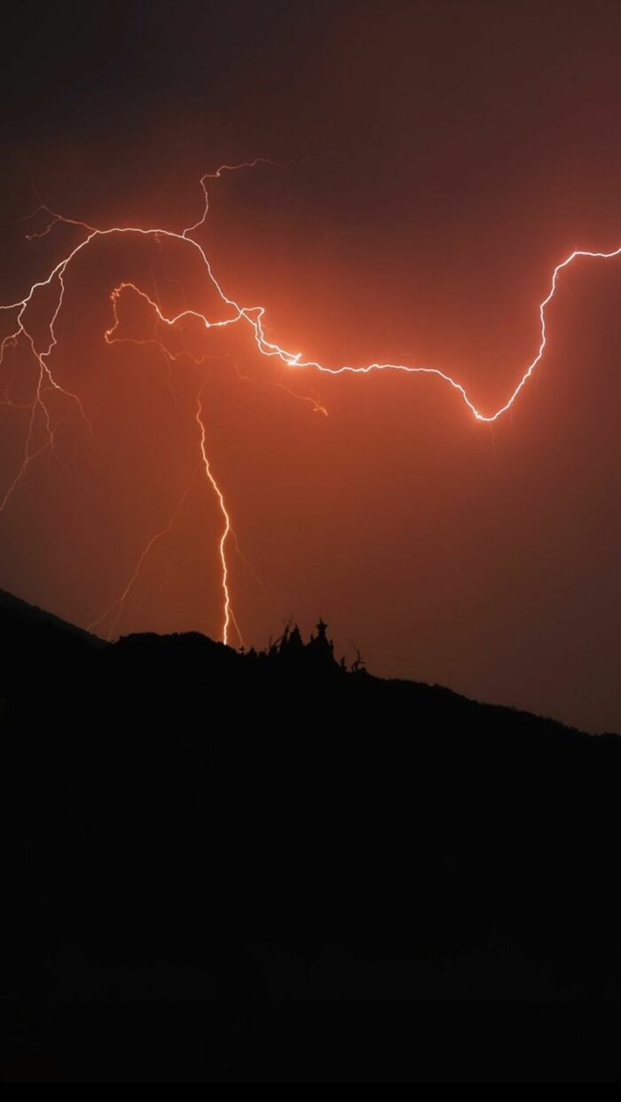 Bright orange lightning striking over a dark mountain, showing a stormy night that makes people leave immediately.