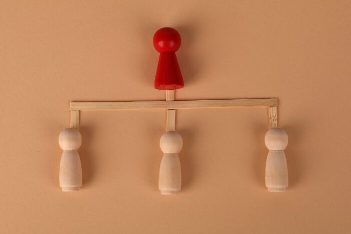 Red wooden game piece positioned above three plain wooden figures on a structure representing corporate structure in companies