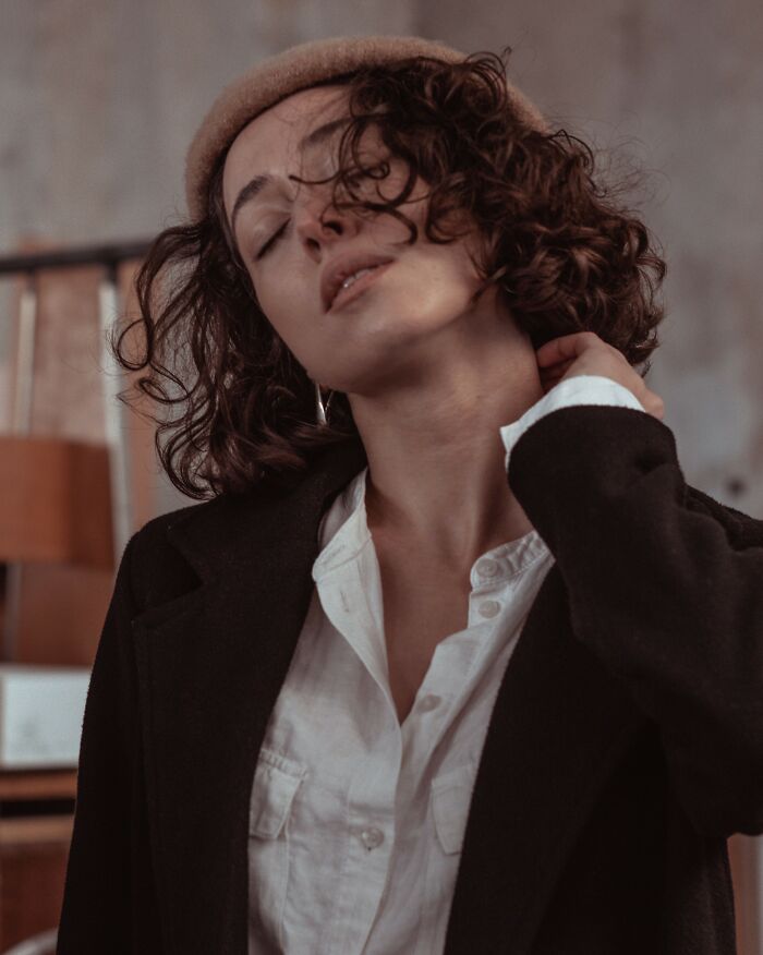 A thoughtful woman with curly hair and a beret wearing a white shirt and black blazer