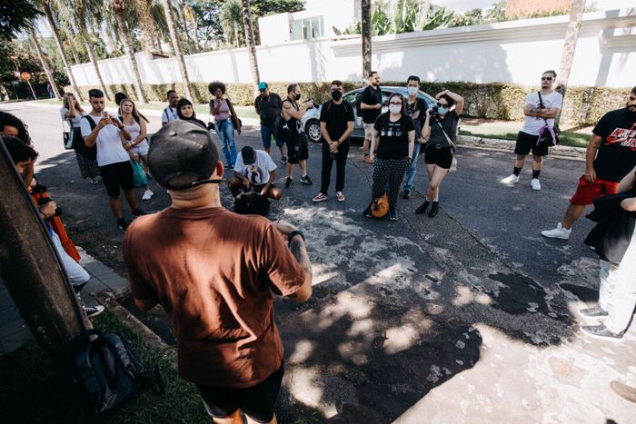 A group of people standing on a street listening to a leader on a paid tour outside a property.