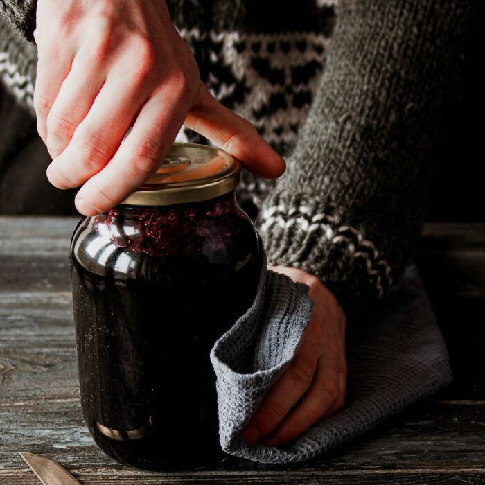 Hand using cloth to grip and open a jar lid on a wooden table