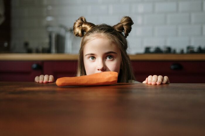 A young girl looking over a table at a raw carrot, expecting candy while trick-or-treating but receiving veggies.