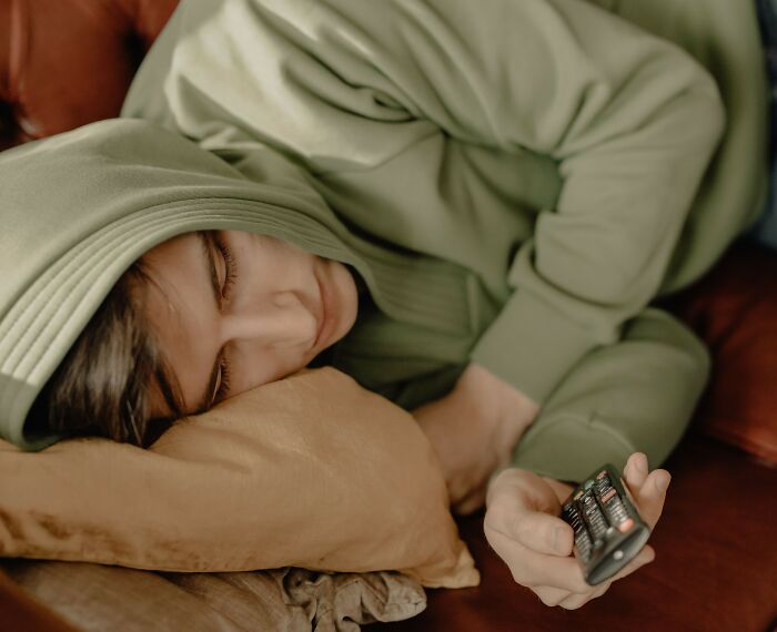 Woman in hoodie resting with remote control, reflecting microaggressions fatigue