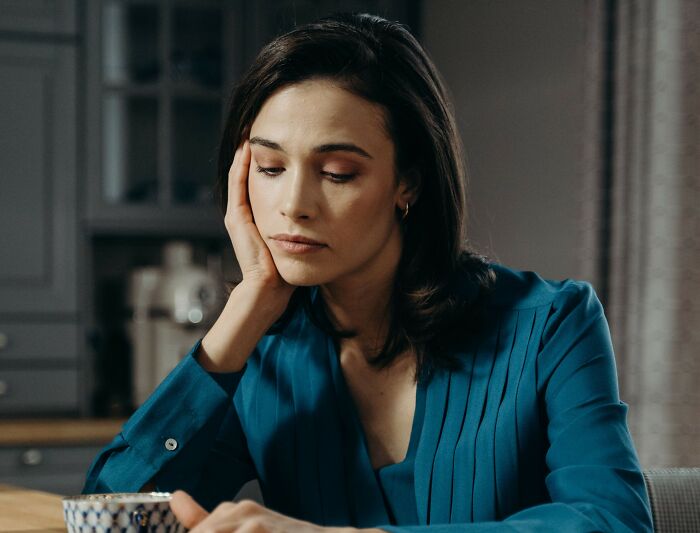 Somber woman sitting at a table with hand on cheek carrying secrets folks hide.