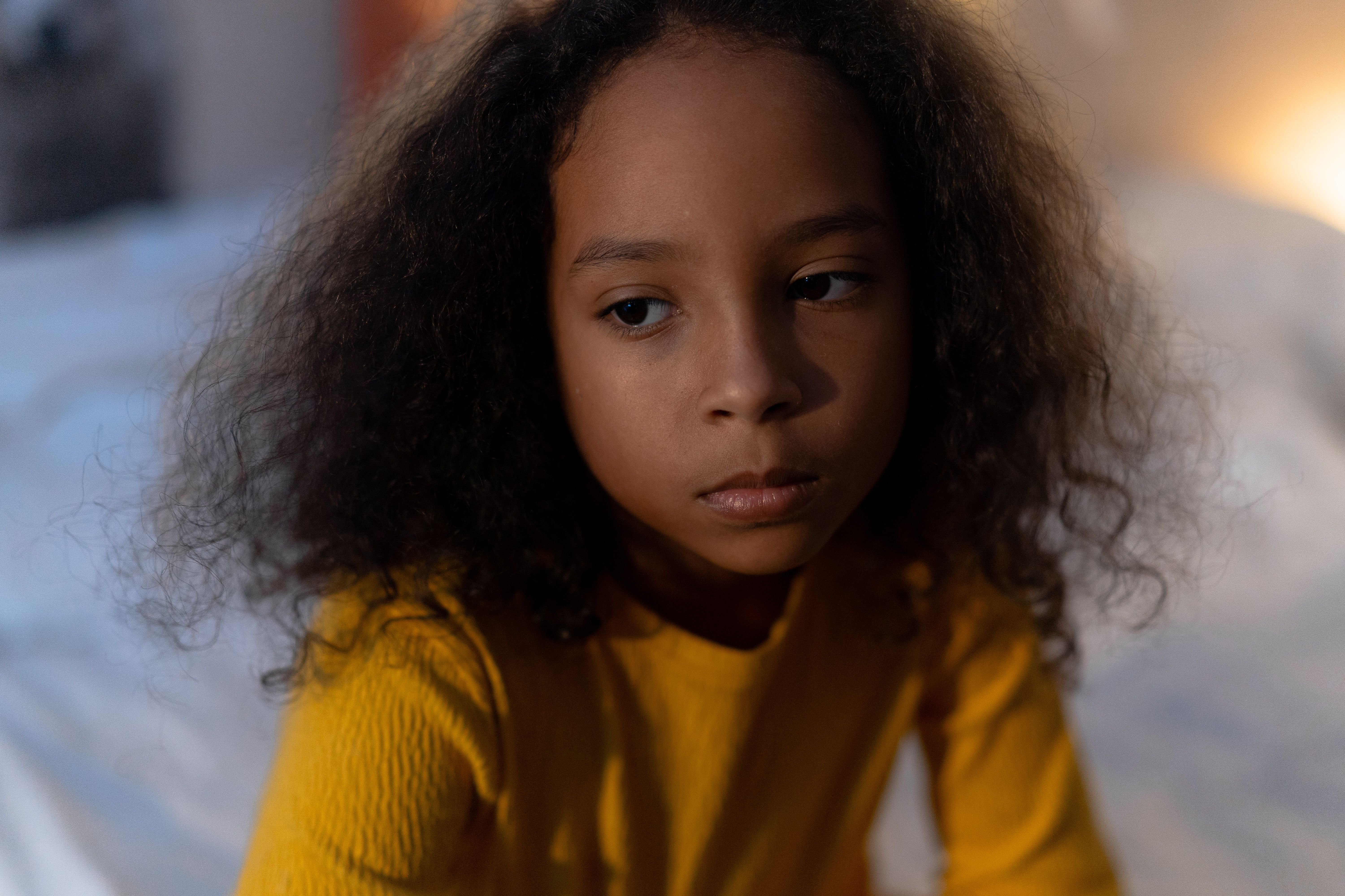 A sad young girl with curly hair looking down, representing a daughter affected by a difficult situation. A sad young girl with curly hair looking down, representing a daughter affected by a difficult situation.