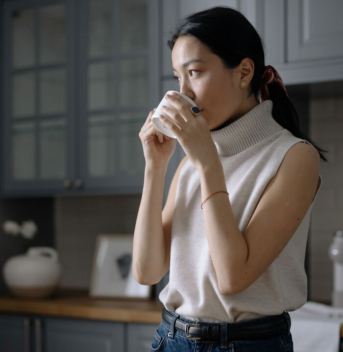 Woman drinking a hot beverage at home while reading about a husband who breaks 5 of wife's ribs by giving her a hug.