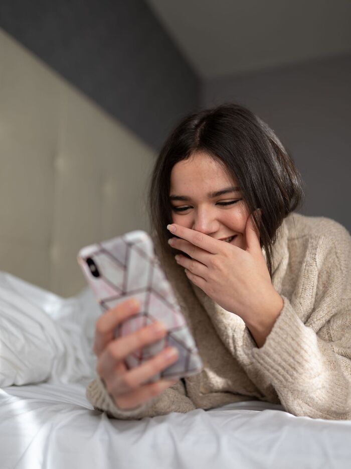 A woman smiling while looking at her phone, depicting a satisfying revenge story