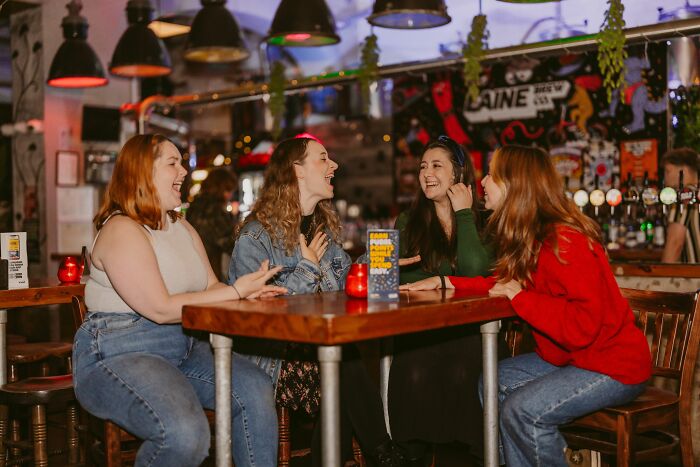 A group of four happy friends laughing together at a bar table, enjoying pub trivia questions