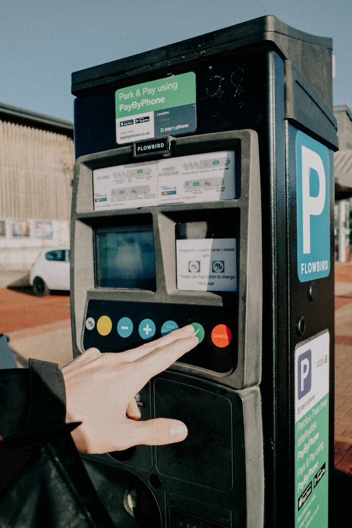 A hand pressing a button on a parking meter machine, demonstrating life tricks for easy urban parking.