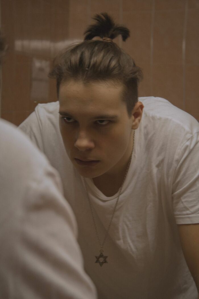 A young man with a hair bun looking in a mirror applying clever life tricks