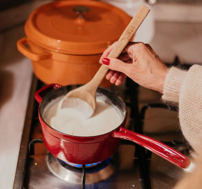 Hand stirring a creamy sauce in a red saucepan on a stove