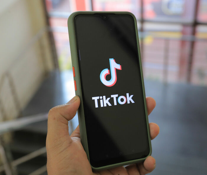 A hand holding a smartphone displaying the TikTok logo, related to the viral Florida Demonologist mugshot A hand holding a smartphone displaying the TikTok logo, related to the viral Florida Demonologist mugshot