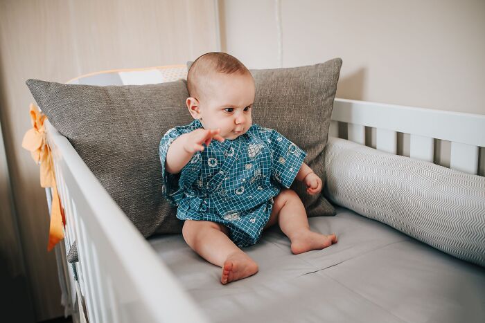 A cute baby sitting in a crib pointing forward, related to funny obvious lies.