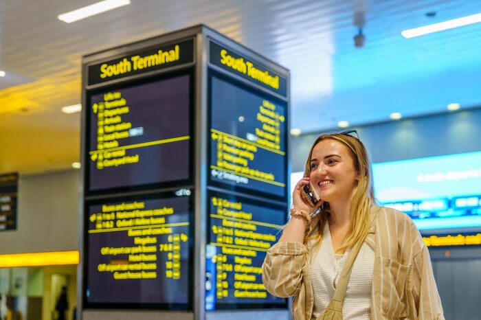 Smiling woman talking on phone at an airport terminal, using clever life tricks to navigate public transit.