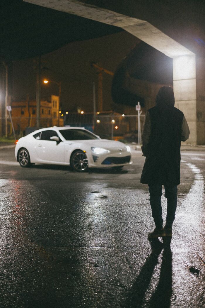 A person standing by a white car at night, evoking the urgent feeling of needing to leave immediately