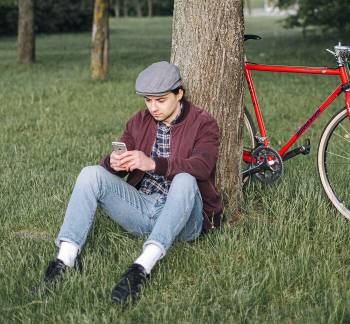 A young man looking at his phone next to a bicycle, highlighting first date communications.