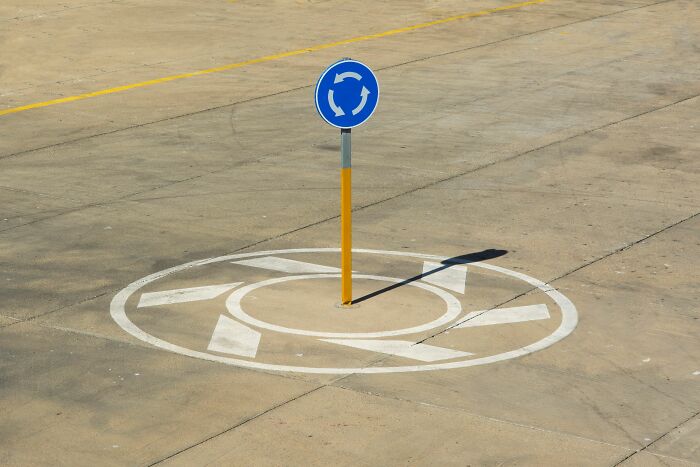 Blue roundabout sign painted on concrete in tiny communities with local news and drama