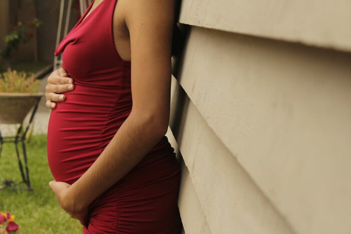 A pregnant woman in a red dress leaning against a wall, touching her belly during a difficult marriage phase.