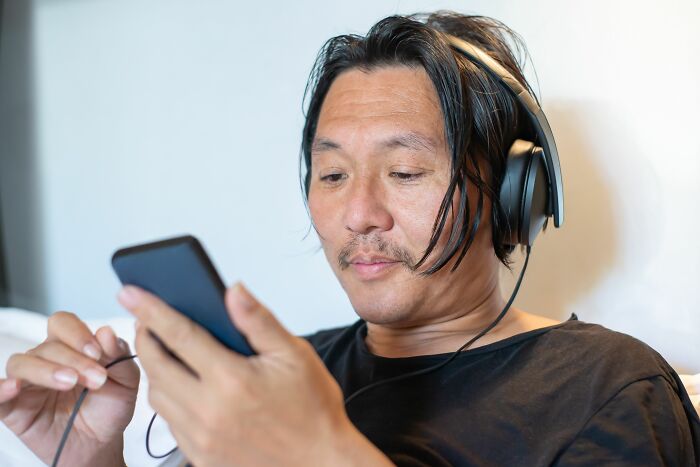 A man wearing headphones using his phone, listening quietly to secrets he keeps from people in his real life.