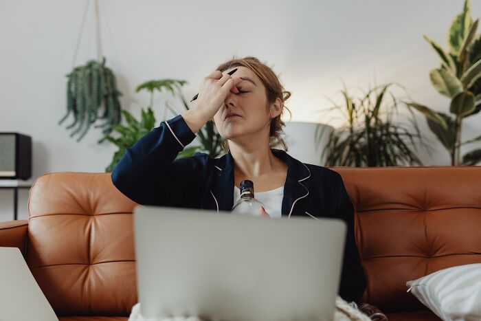 Stressed woman holding her head in front of a laptop, representing behind the scenes struggles at work.