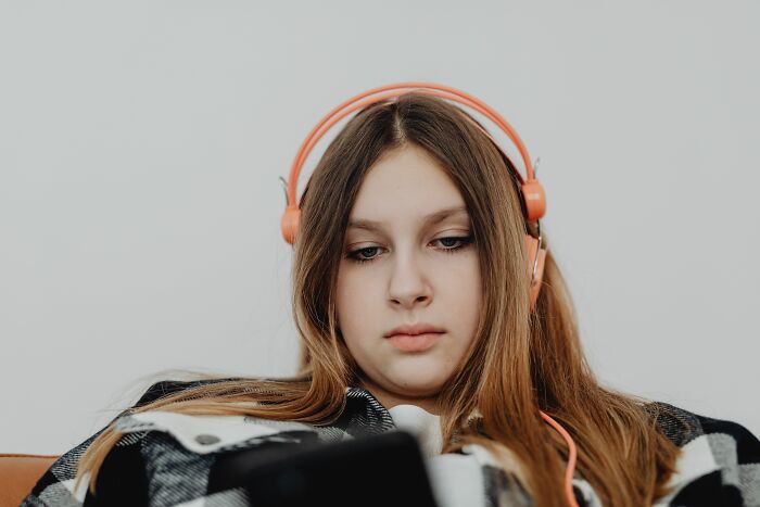 A young woman in orange headphones looking at her phone, reflecting on secret thoughts and personal secrets.