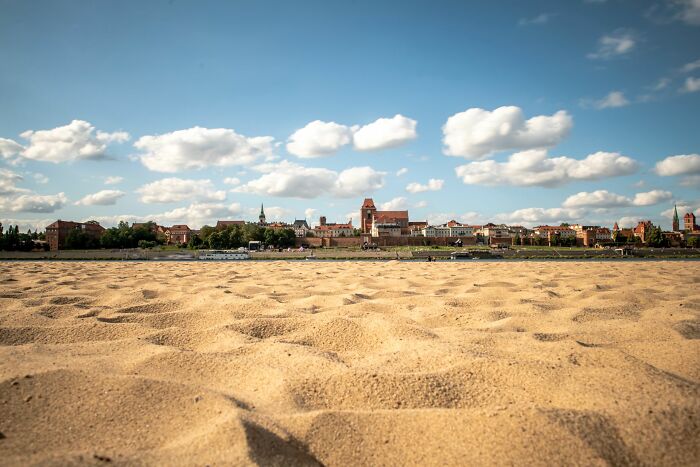 Close-up of sandy beach with city skyline under blue sky