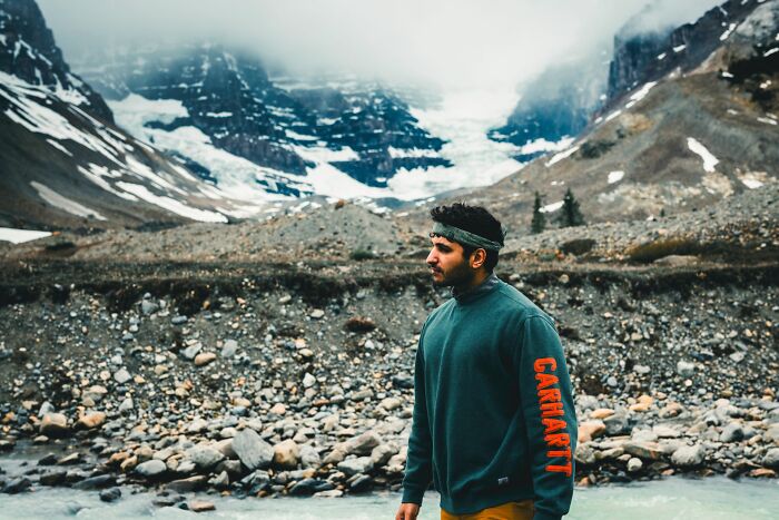 Man wearing a Carhartt sweatshirt standing in front of rocky mountains and glacier