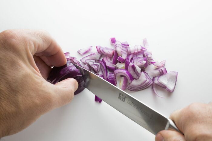 Hands chopping red onion into pieces with kitchen knife