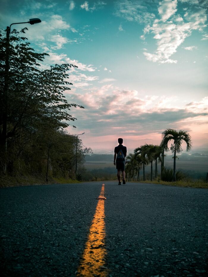 A man walking down a road at sunset, highlighting the urgent feeling to leave immediately.