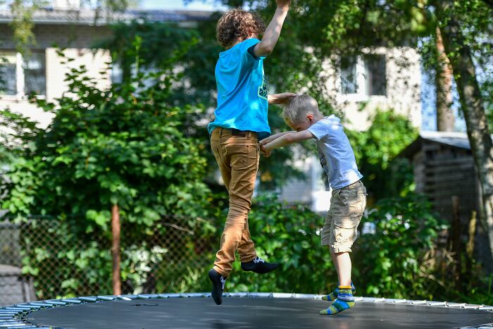 Two boys jumping on trampoline in backyard on sunny day
