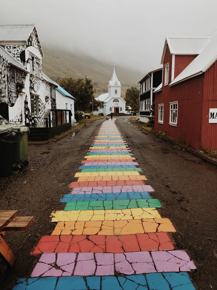 An entertaining pic of a colorful rainbow-painted brick pathway leading to a scenic church