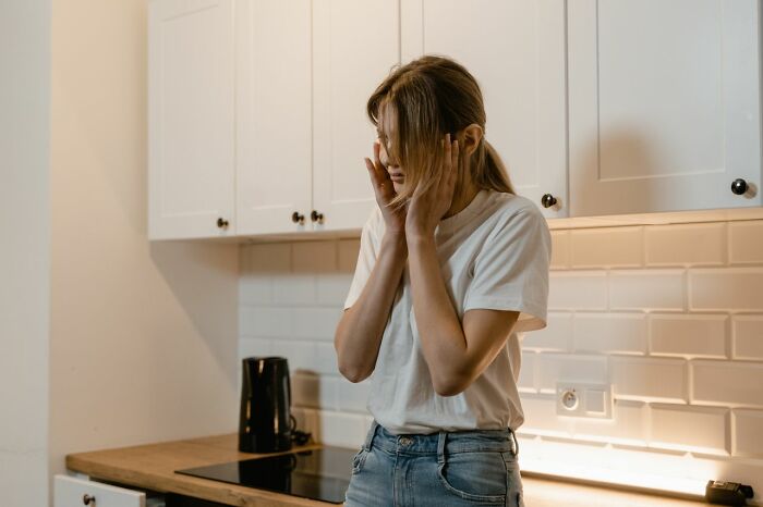 A woman holding her face in distress in a kitchen after funny instances of embarrassing fails.