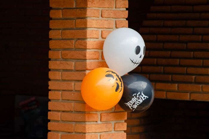 Spooky Halloween balloons with printed scary faces tied to a brick pillar for a Halloween party.
