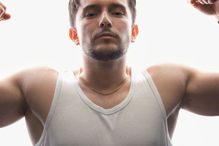 A muscular man in a white tank top flexes his arms, embodying concepts associated with the manosphere.