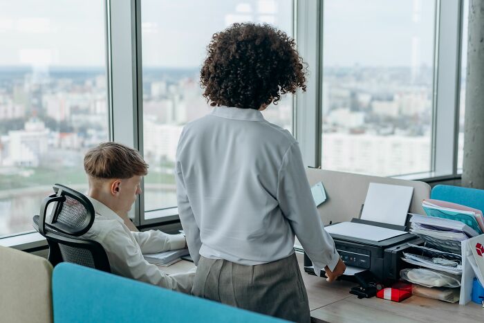 Two coworkers at a printer in an office, discussing things that made partners question their intelligence.