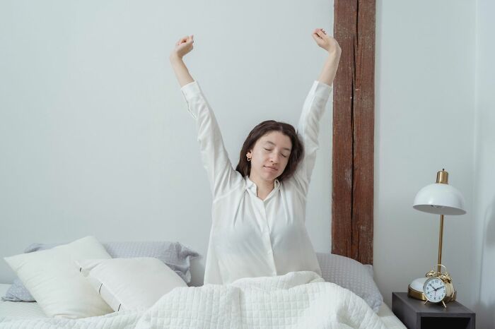 Woman stretching in bed after waking up, demonstrating simple life tricks for a better morning routine.