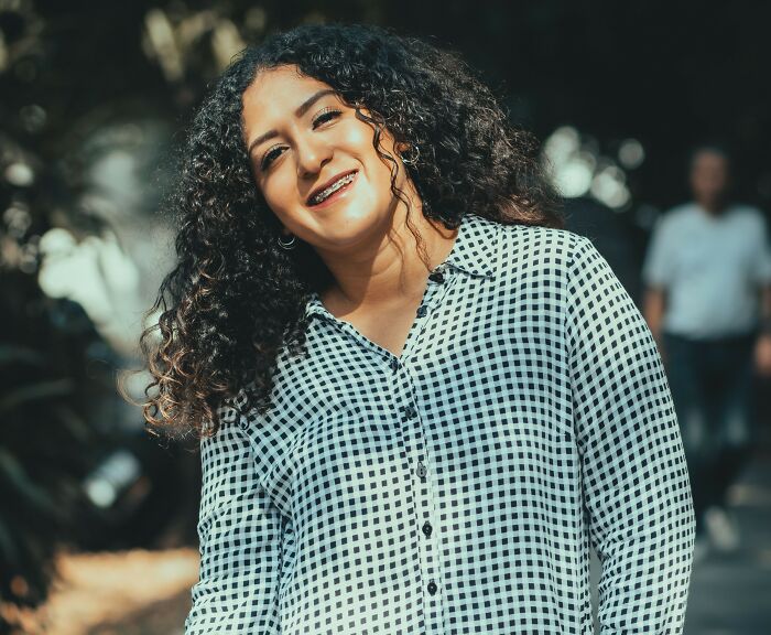 Smiling woman with curly hair wearing a plaid shirt hiding secrets folks carry.