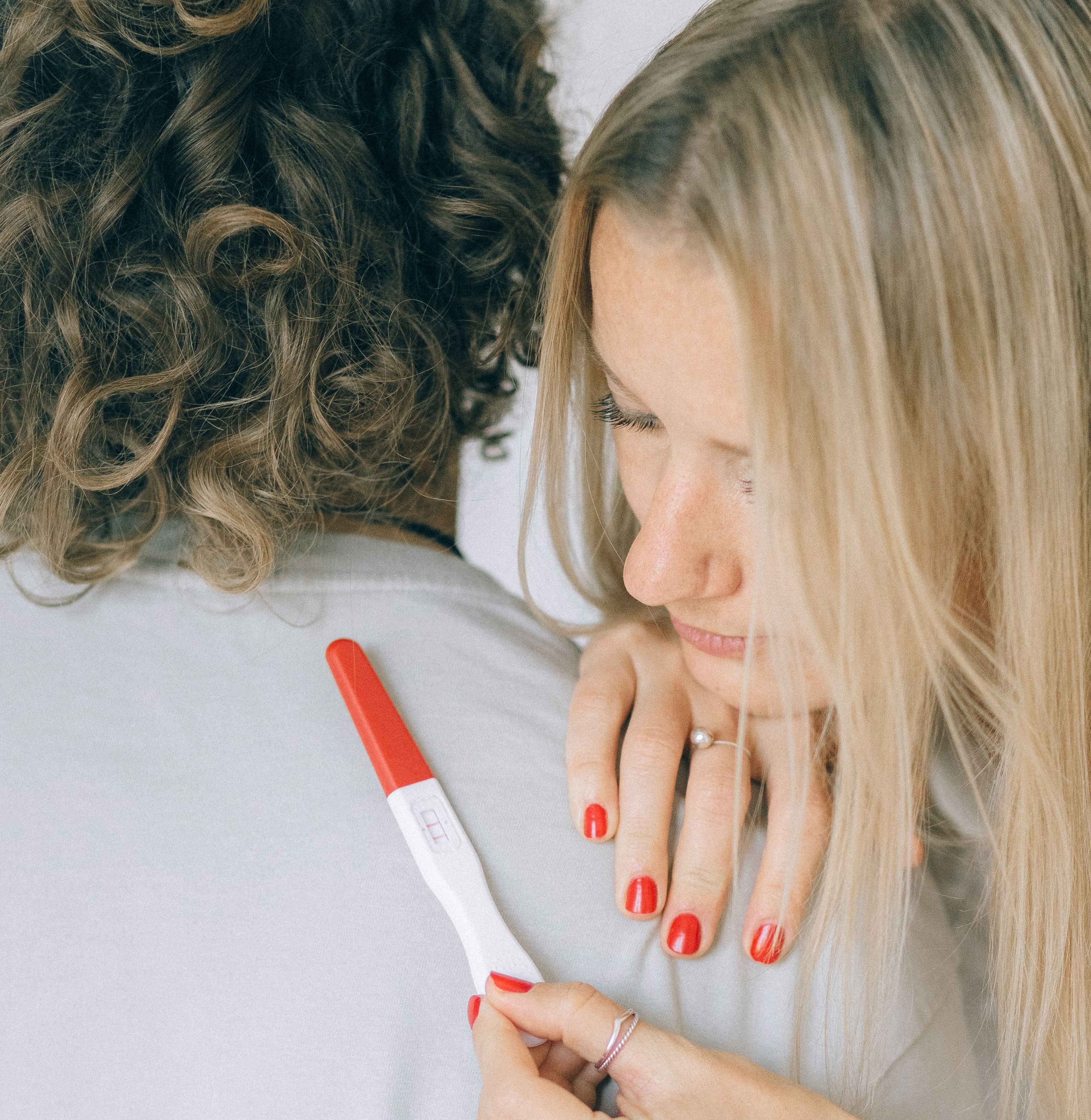 Woman holding a positive pregnancy test while resting her head on her partner's shoulder.